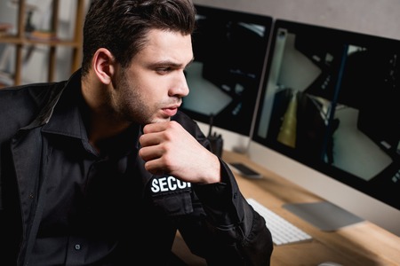 thoughtful guard in uniform looking at computer monitor at workplace