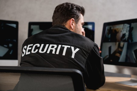 rear view of guard in black uniform looking at computer monitorの写真素材