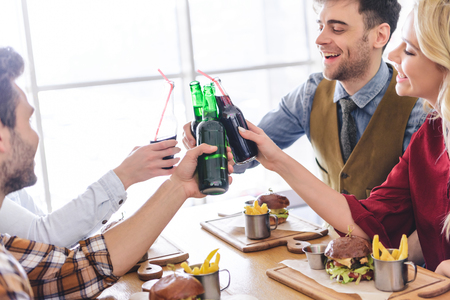 handsome and beautiful friends cheering with glass bottles and smiling at cafeの写真素材