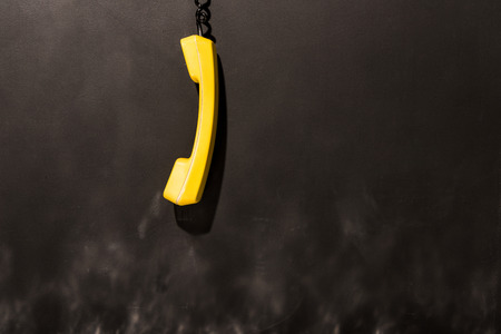 Yellow handset with black wire hanging on dark backgroundの写真素材