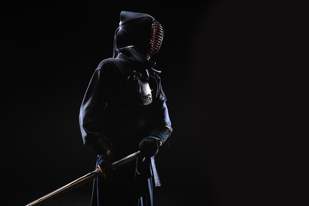 Kendo fighter in helmet holding bamboo sword on blackの写真素材