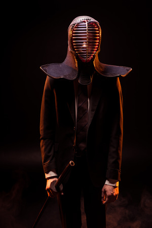 Man in suit and kendo helmet holding bambo sword on blackの写真素材