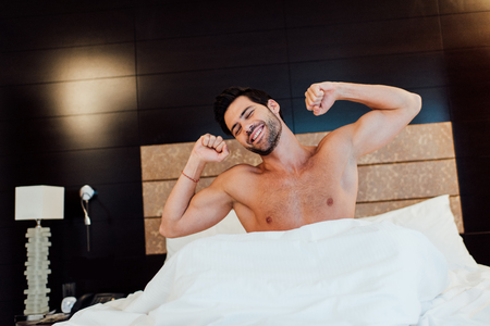 cheerful muscular man stretching in bed after wake upの写真素材