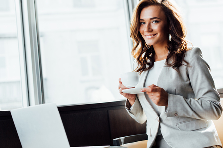 cheerful businesswoman holding cup of coffee and looking at cameraの写真素材
