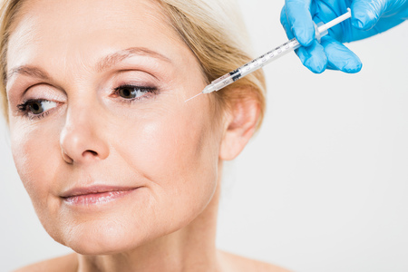 beautiful and mature woman getting beauty injection and looking away isolated on grey