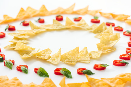 selective focus of tasty nachos and chili peppers with basil on white background