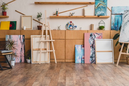 spacious light painting studio with wooden cabinets, shelves, easels and paintingsの写真素材