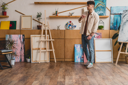 good-looking artist in pink shirt and blue jeans standing in spacious light galleryの写真素材