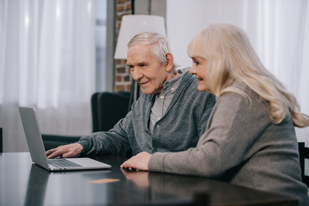 happy senior couple sitting at table and using laptop at homeの写真素材