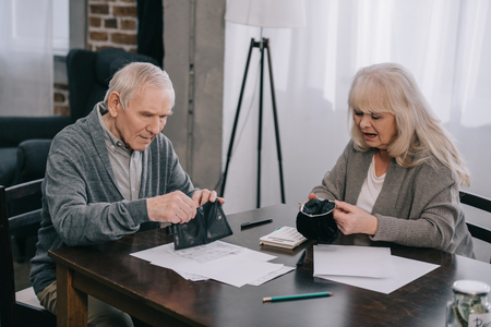 senior couple holding wallets while sitting at table with documentsの写真素材