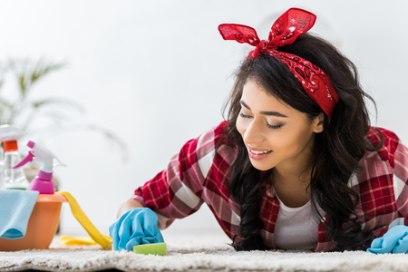 pretty african american woman in plaid shirt cleaning carpetの写真素材