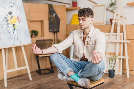 selective focus of dreamy artist with closed eyes sitting in lotus pose in galleryの写真素材