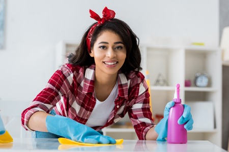 smiling african american woman with yellow rag and pink spray bottle looking at cameraの写真素材