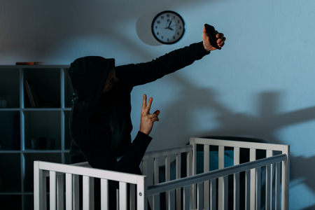 Kidnapper taking selfie near crib and showing peace signの写真素材