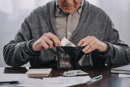 cropped view of male pensioner sitting at table with paperwork and putting money in walletの写真素材