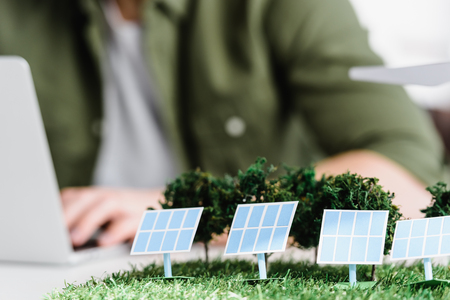 selective focus of solar panels and trees models on table near architect in officeの写真素材