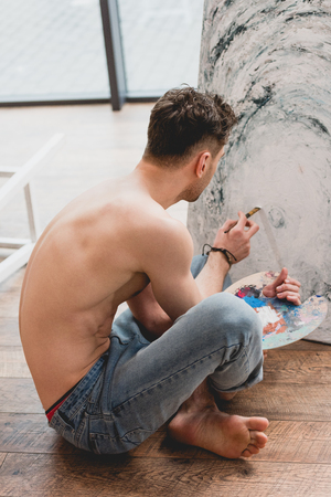 half-naked artist sitting with crossed legs and painting picture in galleryの写真素材