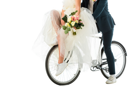 partial view of bride with wedding bouquet sitting on bicycle together with groom isolated on whiteの写真素材