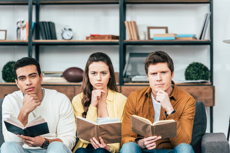 Three multicultural students sitting on sofa and reading books in living roomの写真素材