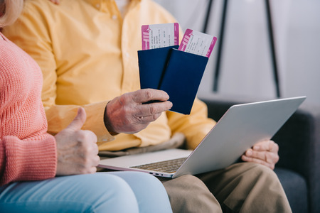 cropped view of senior couple showing thumb up sign and holding air tickets with passports