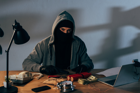 Criminal in mask with gun and dynamite sitting at table and looking at cameraの写真素材