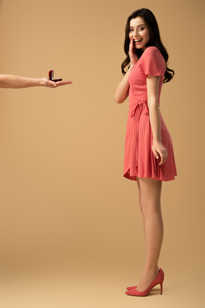 Cropped view of man making marriage proposal to surprised brunette girl in dress on beige backgroundの写真素材