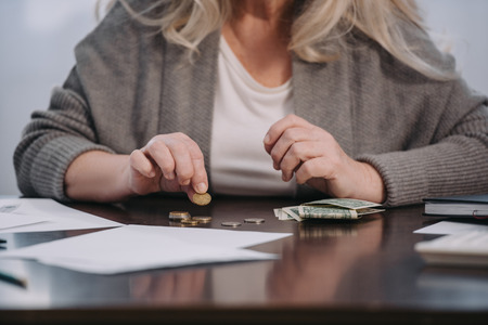 cropped view of female pensioner sitting at table and counting money at homeの写真素材