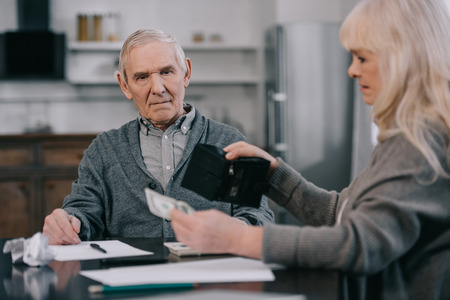 senior woman holding wallet and money while sitting at table with manの写真素材