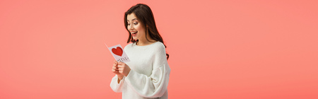 panoramic shot of surprised young woman holding card with love lettering isolated on pinkの写真素材