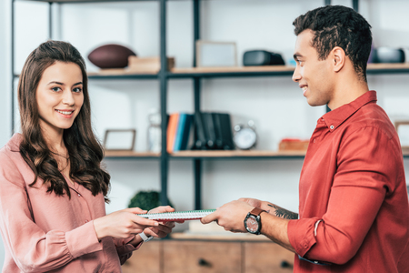 Two smiling multicultural students holding bright notebooks together at homeの写真素材