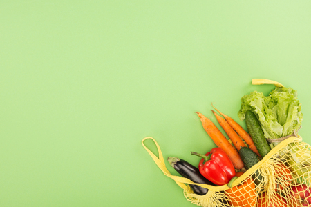 red bell pepper, carrots, lettuce, cucumbers and eggplant in yellow string bag on light green backgroundの写真素材