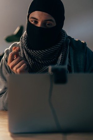 Happy terrorist in mask looking at webcam and showing money gestureの写真素材