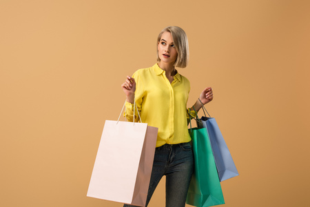 Pensive blonde girl in yellow shirt holding shopping bags isolated on beigeの写真素材