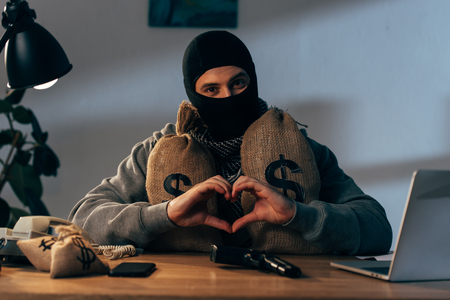 Terrorist in mask with money bags showing heart sign