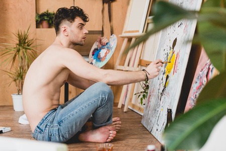 selective focus of thoughtful half-naked artist holding palette and painting pictureの写真素材