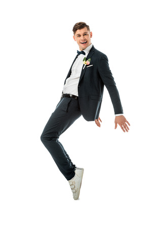 cheerful groom dancing in black suit and white sneakers isolated on whiteの写真素材