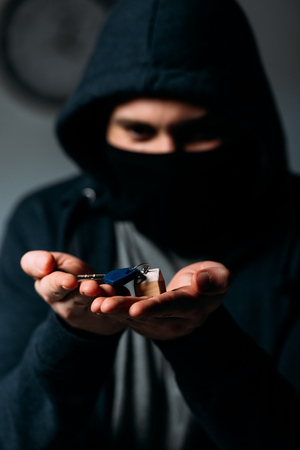 Criminal in black hoodie and mask showing keys at cameraの写真素材