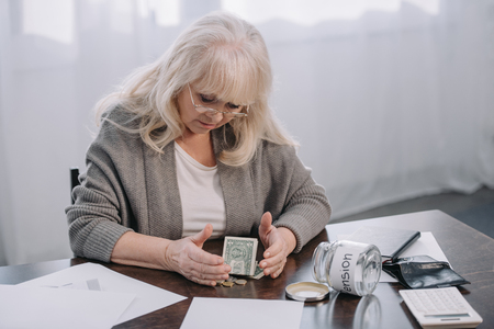 senior woman sitting at table with money, paperwork and empty glass jar with 'pension' wordの写真素材
