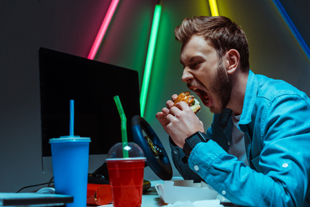 selective focus of handsome and good-looking man eating tasty burgerの写真素材