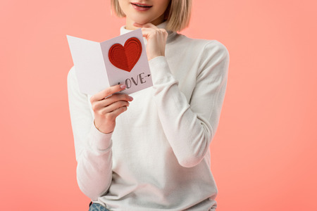 cropped view of woman holding greeting card while standing isolated on pinkの写真素材