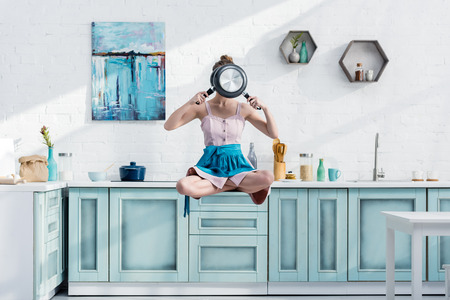 young woman flying in air in lotus pose with pans in front of faceの写真素材
