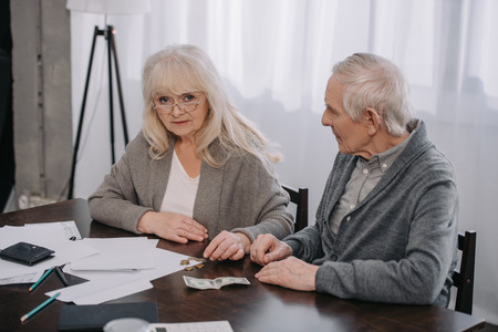 senior couple sitting at table with paperwork while counting money