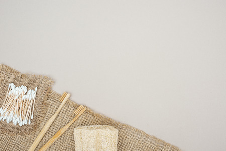 bamboo toothbrushes, organic loofah, cotton swabs and brown sackcloth on grey background