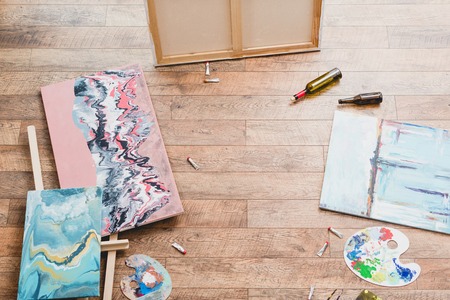 high angle view of paintings, draw utensils and empty bottles on wooden floor in painting studio
