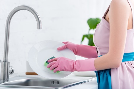 cropped view of young woman in pink rubber gloves washing dishes in kitchenの写真素材