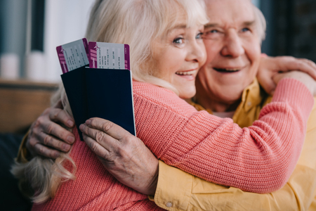 smiling senior couple hugging and holding air tickets with passports at homeの写真素材