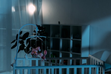 Crib and pink mobile with toys in dark nurseryの写真素材