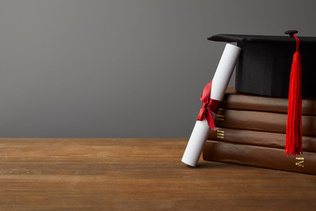 Diploma, academic cap and books on wooden surface isolated on greyの写真素材