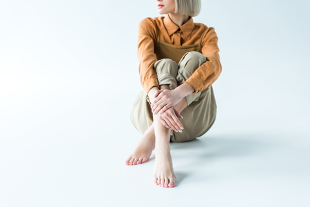 cropped view of stylish young woman sitting with crossed legs on whiteの写真素材