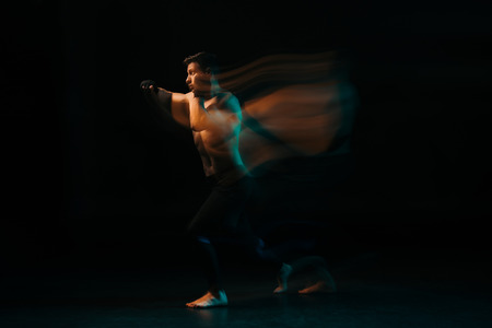 long exposure of orange and green light and shirtless muscular mma fighter doing punch